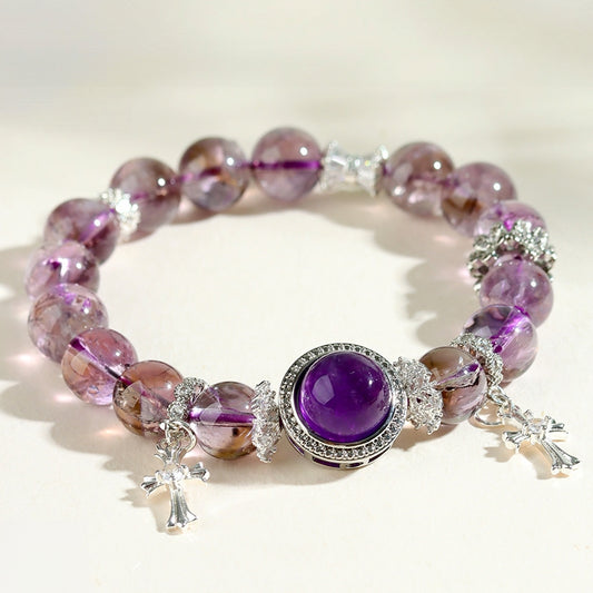 Close-up of phantom amethyst bead bracelet with silver cross pendants on a warm white surface — luminous purple tones, dreamy and ethereal