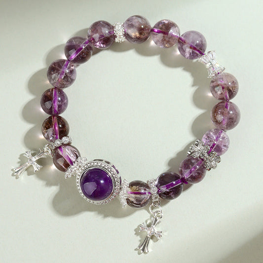 Phantom amethyst bracelet with silver cross charms on a soft neutral surface — deep purple and translucent beads catching natural light, mystical and refined